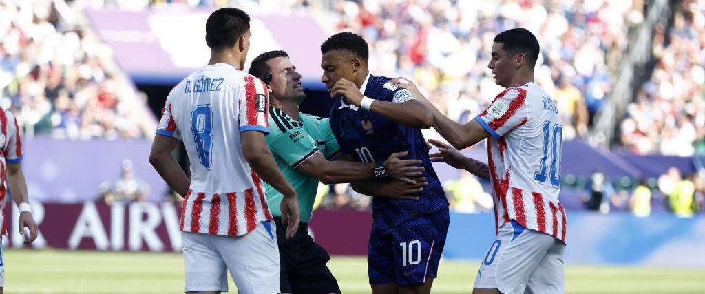 El árbitrto Ilgiz Tantashev contiene a Mbappé mientras discute contra jugadores paraguayos. 
