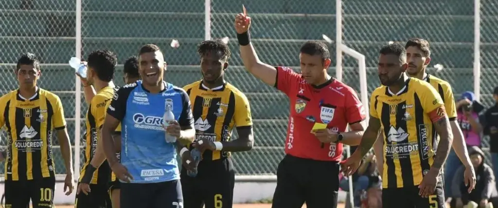 El árbitro Gery Vargas (centro) le muestra la tarjeta roja al defensor de Blooming Julio Vila. 